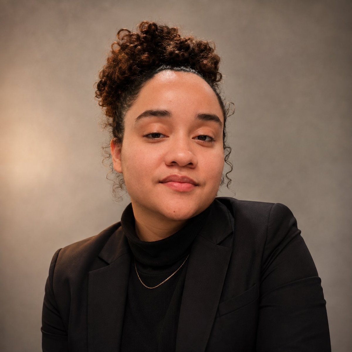 Founder of Alves Solutions with curly reddish-brown hair styled up, wearing a black blazer and gold chain necklace against a neutral beige background